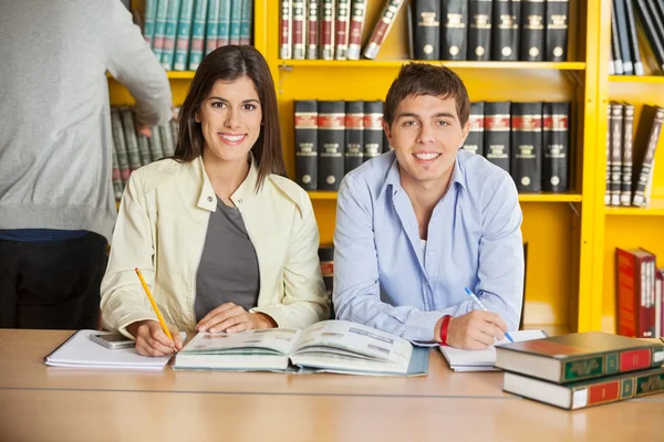 Estudiantes universitarios con libros sentados a la mesa en la biblioteca —  Fotos de Stock