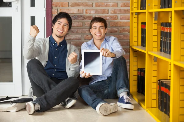 Estudiantes masculinos mostrando tableta digital mientras están sentados en la biblioteca —  Fotos de Stock