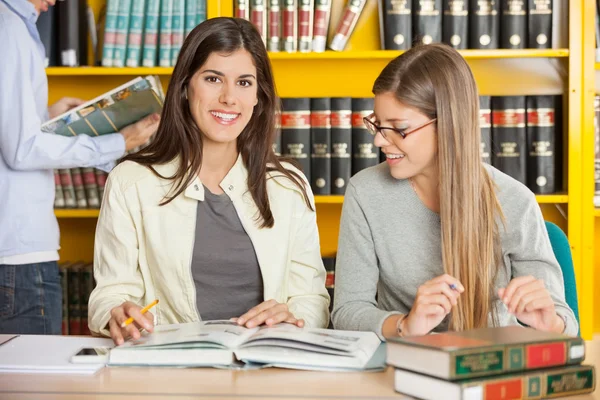 Kvinnlig student med vän sitter i biblioteket — Stockfoto
