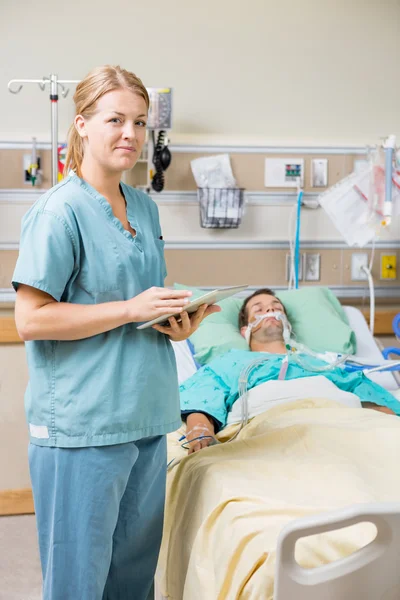 Медсестра с цифровой таблеткой в то время как мужчина Пациент отдыхает на кровати — стоковое фото