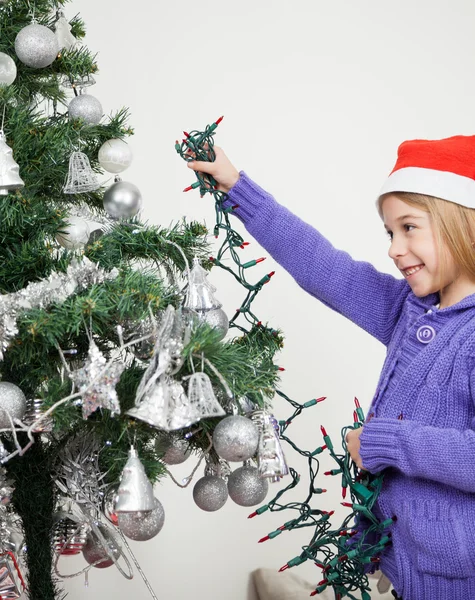 Chica decorando el árbol de Navidad con luces de hadas —  Fotos de Stock