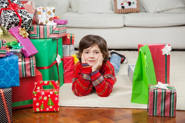 Halmozott karácsonyi ajándékok mellett fekvő fiú — Stock Fotó