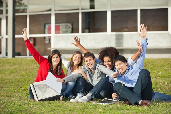 Studenti con le mani alzate seduto al campus universitario — Foto Stock