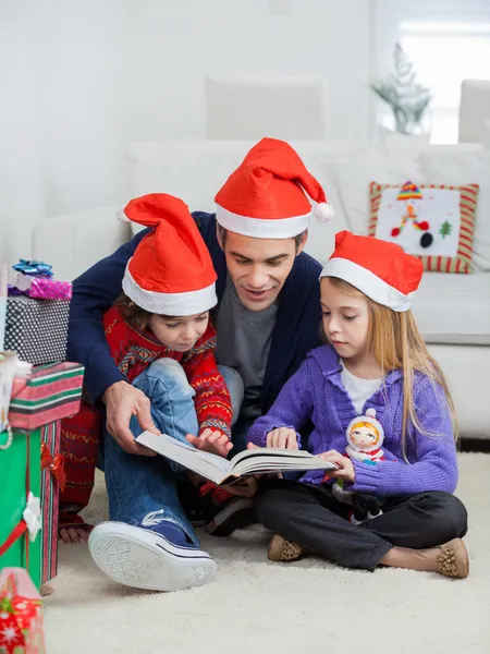 Vater und Kinder in Weihnachtsmützen lesen Buch — Stockfoto