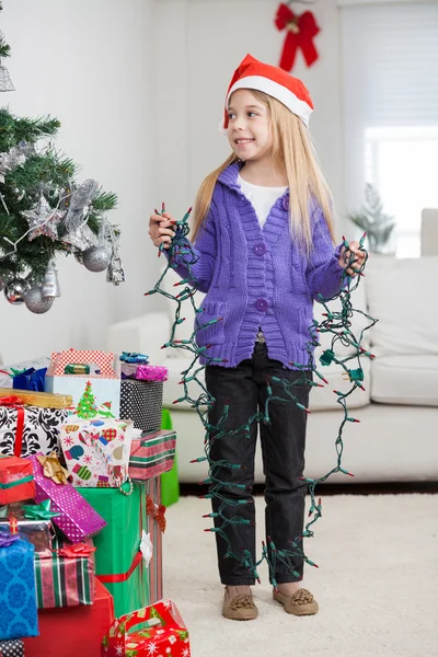 Chica sosteniendo luces de hadas mientras está de pie por regalos de Navidad —  Fotos de Stock