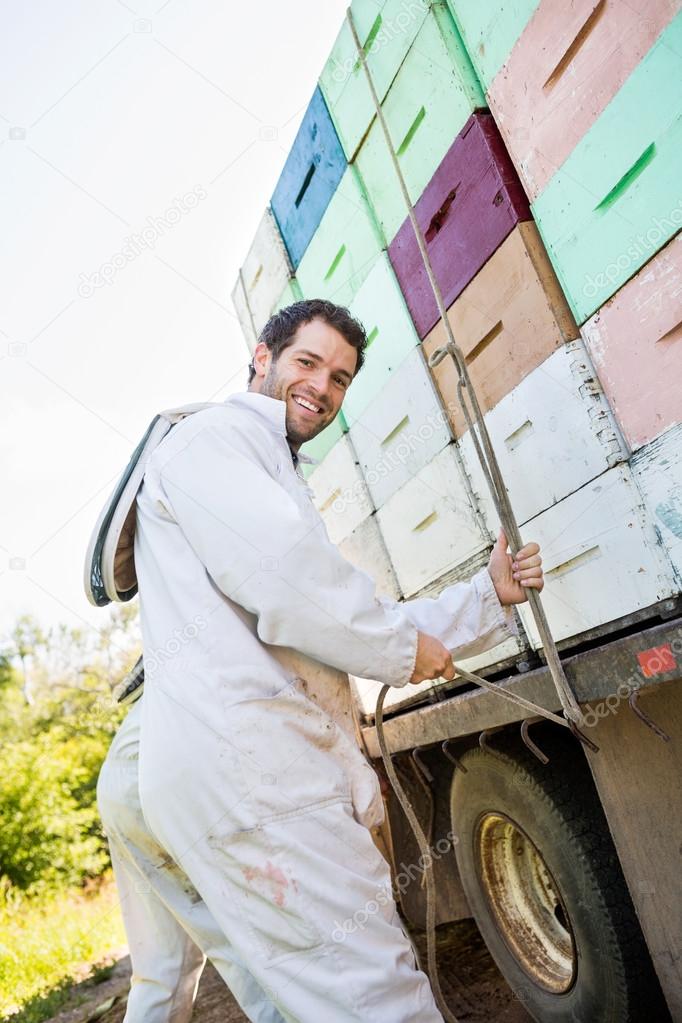 Beekeeper Tying Rope Stacked Honeycomb Crates On Truck