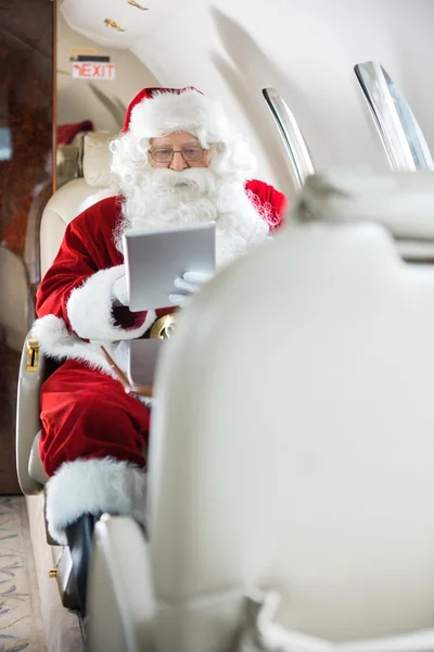 Santa met behulp van tablet pc in prive-jet — Stockfoto