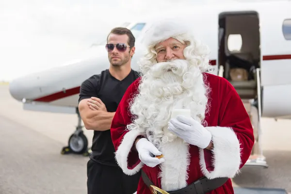 Santa Holding Milk Glass by Bodyguard Against Private Jet — стоковое фото