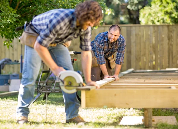 Carpenter Looking At Coworker While Assisting Him In Cutting Woo — Stock Photo, Image