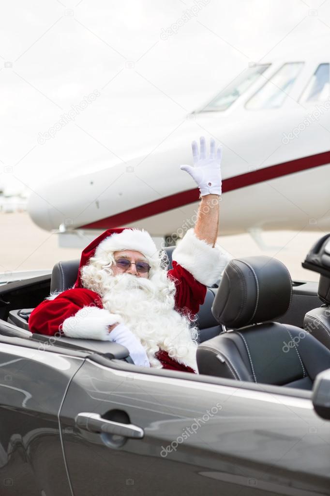 Santa Waving Hand In Convertible Against Private Jet