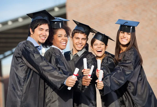 Estudiantes en vestidos de graduación mostrando diplomas en el campus —  Fotos de Stock