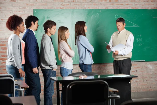 Professore con risultati degli esami mentre gli studenti sono in piedi alla scrivania — Foto Stock