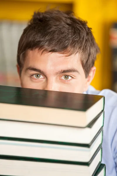 Student prohlížení přes hromadu knih v univerzitní knihovně — Stock fotografie