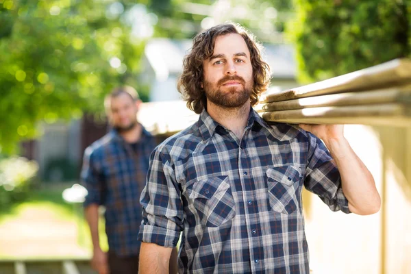 Carpinteiro com colega transportando tábuas de madeira ao ar livre — Fotografia de Stock
