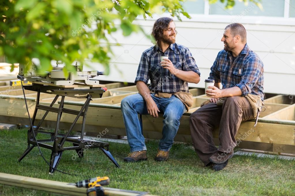 Carpenters With Disposable Cups Looking At Each Other On Frame