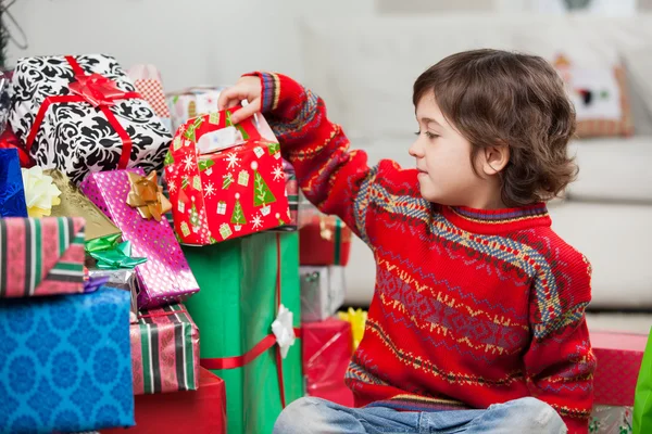 Menino sentado por presentes de Natal empilhados — Fotografia de Stock