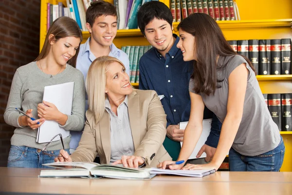 Leraar bespreken met studenten aan tafel in de bibliotheek van de Universiteit — Stockfoto