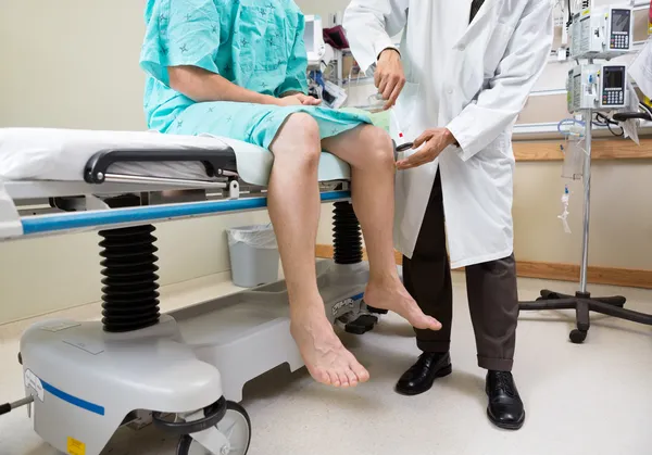 Neurólogo examinando rodilla de paciente con martillo en hospital — Foto de Stock