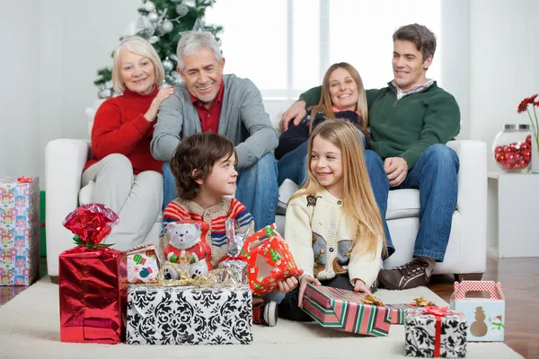 Crianças com presentes de Natal enquanto a família está sentada no sofá — Fotografia de Stock