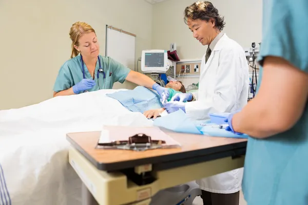 Doutor costurando ferida do paciente masculino enquanto enfermeira assistindo-o — Fotografia de Stock