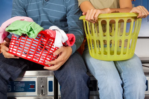 Pareja con cestas de lavandería sentada en lavadoras — Foto de Stock