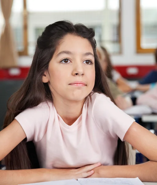 Задумчивая школьница смотрит в сторону, сидя за столом — стоковое фото