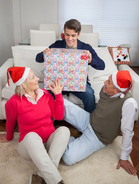 Hombre sosteniendo regalo de Navidad mientras los padres lo miran —  Fotos de Stock