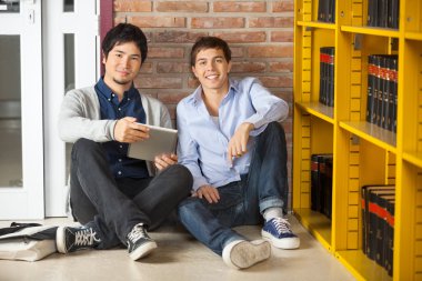 Öğrenciler üniversite kitaplığında oturan dijital tablet ile