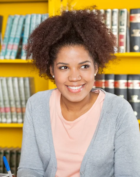 Femme regardant loin tout en souriant à la bibliothèque universitaire — Photo