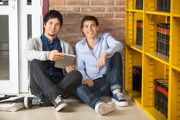 Estudiantes con tableta digital sentados en la biblioteca universitaria —  Fotos de Stock