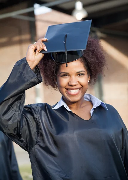 Студент в выпускном платье носит миномётную доску на кампусе — стоковое фото