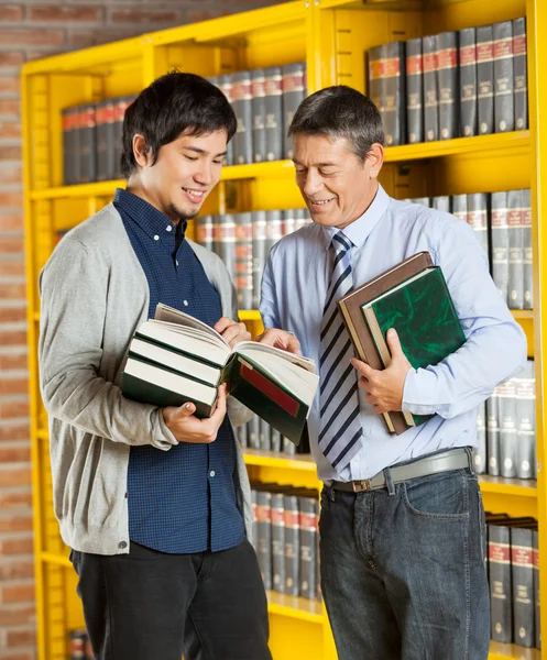 Bibliotecario sosteniendo libros mientras explica al estudiante en la biblioteca — Foto de Stock