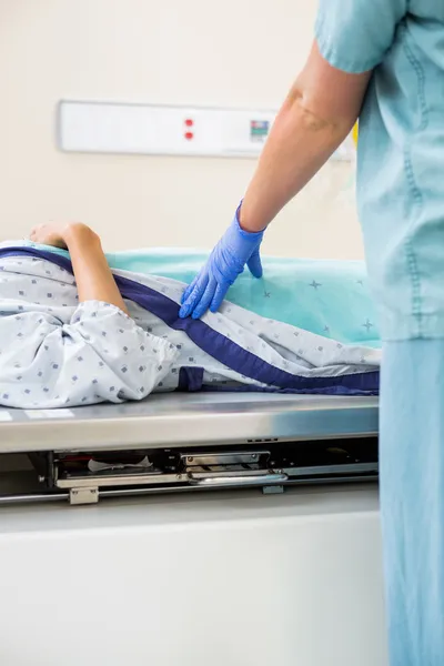 Enfermera de pie junto al paciente acostada en la mesa de rayos X — Foto de Stock