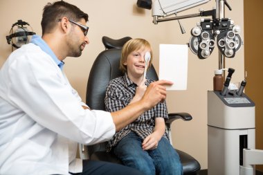 Boy Covering Eye with Occluder at Optometrist clipart