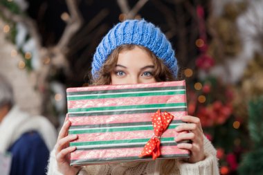 Woman Covering Face With Christmas Present At Store