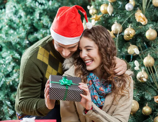 Glückliches Paar hält Geschenk gegen Weihnachtsbaum — Stockfoto