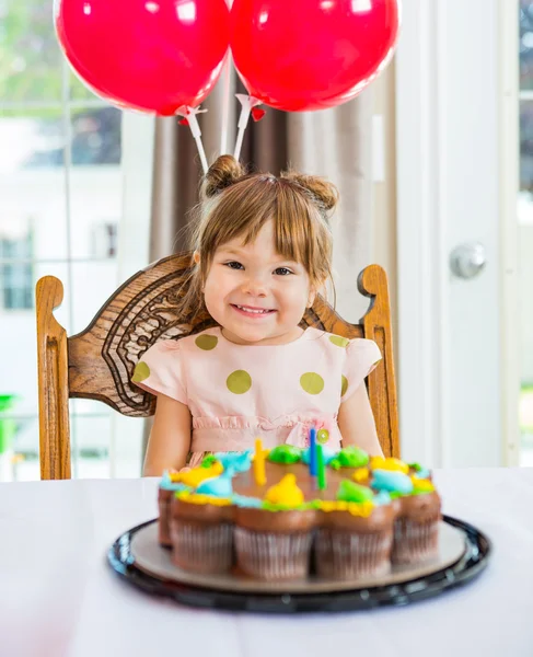 Felice ragazza seduta di fronte alla torta a casa — Foto Stock