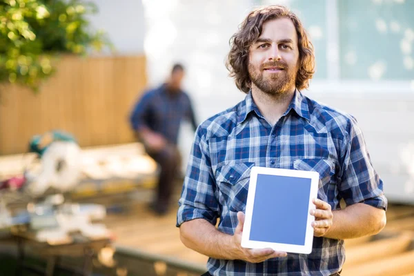 Carpenter Displaying Tablet Computer With Coworker Working In Ba — Stock Photo, Image