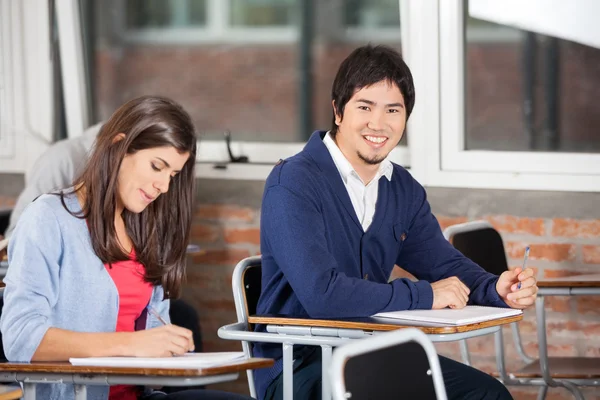 Studente seduto alla scrivania con compagno di classe in aula — Foto Stock