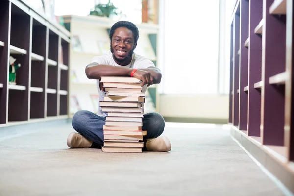 Vertrouwen student met gestapelde boeken zit in bibliotheek — Stockfoto