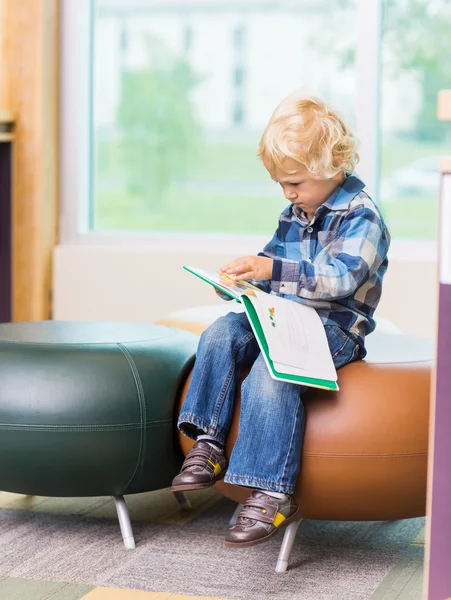 Bonito menino leitura livro no escola biblioteca — Fotografia de Stock