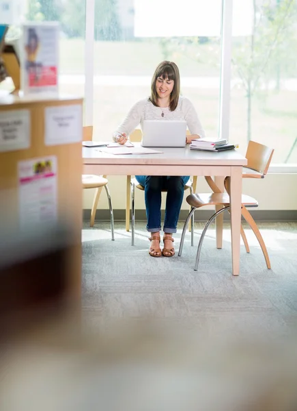 Student met laptop schrijven nota's in bibliotheek — Stockfoto