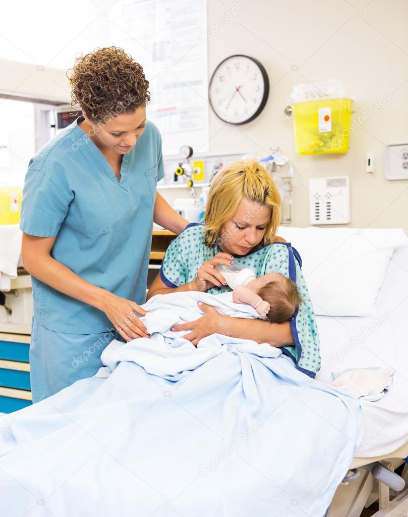 Nurse Looking At Patient Feeding Milk To Baby At Hospital