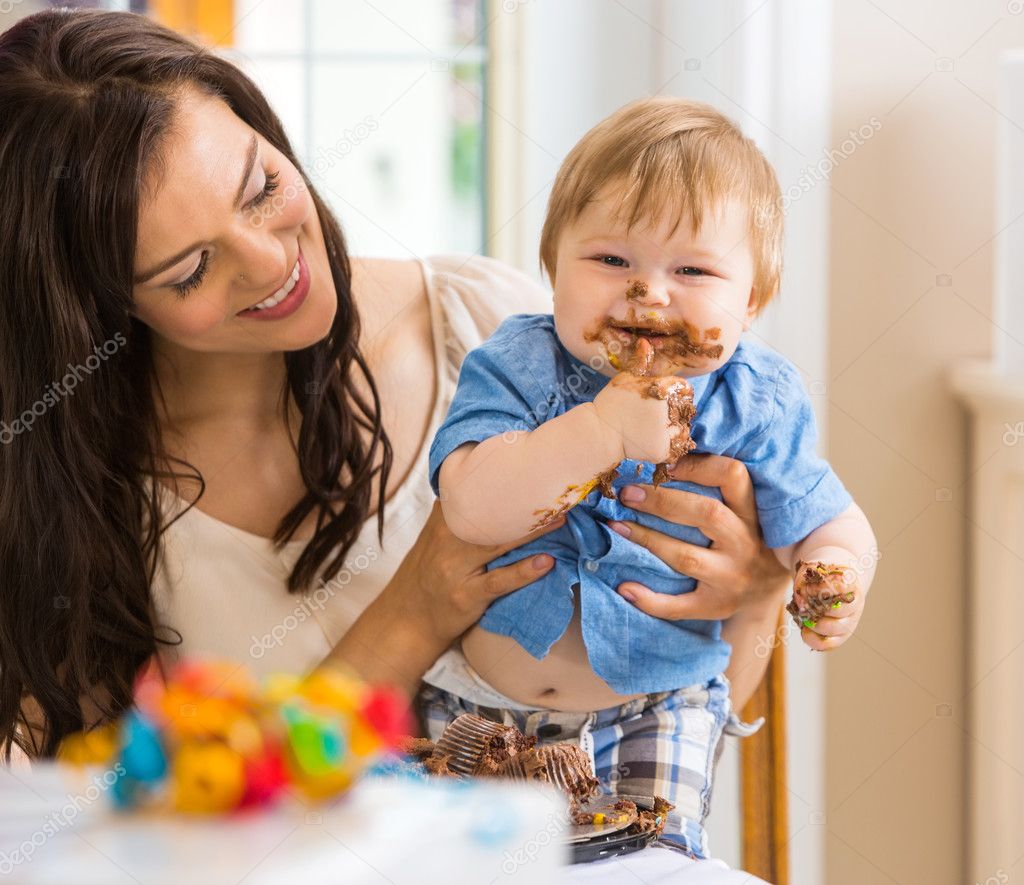 Mother Holding Baby Boy Eating Cake With Icing On Face
