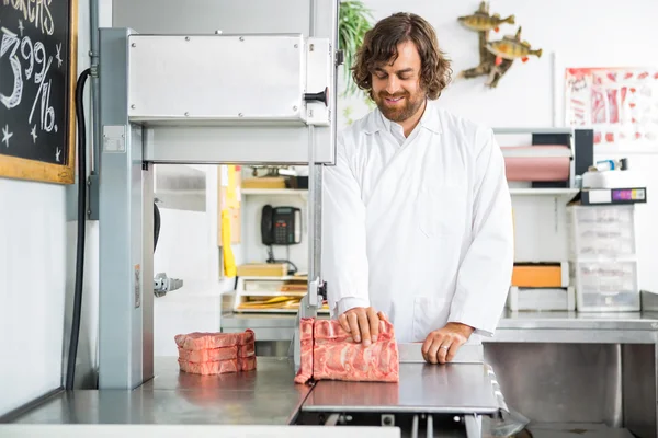 Sourire boucher tranchant la viande dans la machine — Photo