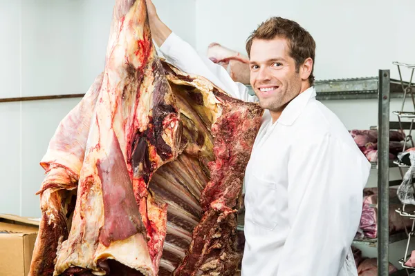 Metzger steht in Kühlbox neben Rindfleisch — Stockfoto