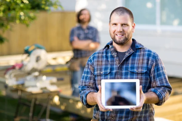 Carpintero mostrando tableta digital con compañero de trabajo en segundo plano —  Fotos de Stock
