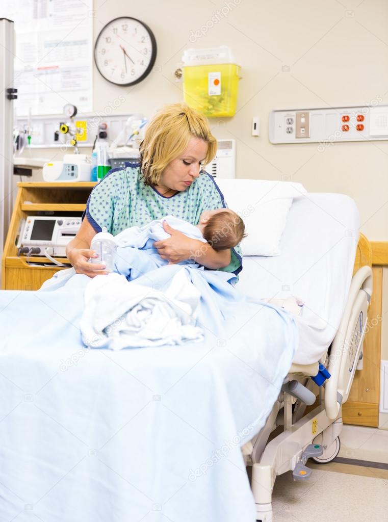 Mother Looking At Newborn Baby While Sitting In Hospital Bed