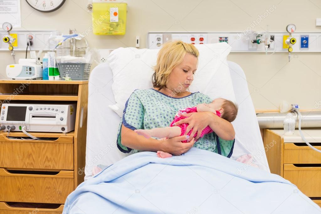 Mother Looking At Newborn Baby Girl While Sitting On Bed