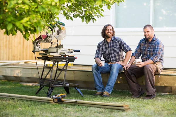 Carpenters Holding Disposable Cups While Sitting On Wooden Frame — Stock Photo, Image